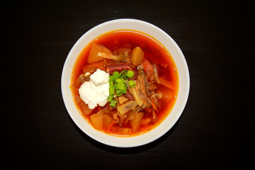 Borscht soup in a white bowl on dark wooden background. Top view. Famous traditional Ukrainian and Russian borshch soup with beetroot and cabbage. Red Eastern Europe soup.