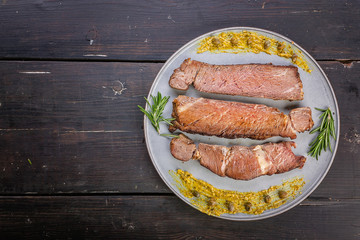 Beef steaks with spices and sauce on a round gray plate on a dark wooden background. Top view. Copy sapce
