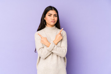 Young indian woman isolated on purple background points sideways, is trying to choose between two options.