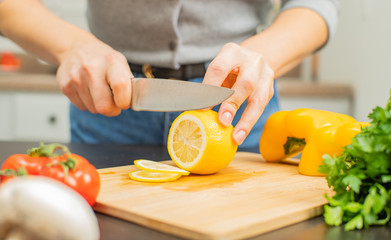 Woman is cutting lemon on kitchen table.