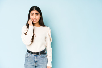 Young indian woman isolated on blue background biting fingernails, nervous and very anxious.