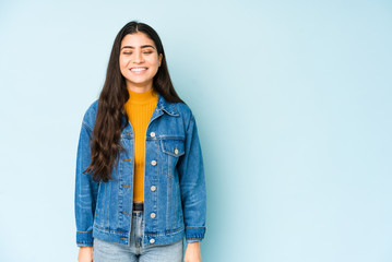 Young indian woman isolated on blue background laughs and closes eyes, feels relaxed and happy.