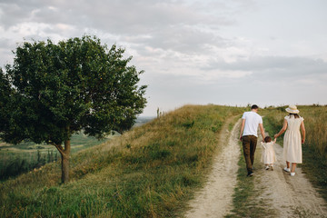 Family, mom, dad, daughter are walking on a hill in the field. Mom and daughter in yellow identical dresses.