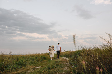 Family, mom, dad, daughter are walking on a hill in the field. Mom and daughter in yellow identical dresses.