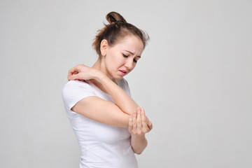 A girl in a white T-shirt massages her elbow from acute pain in the joint.