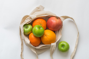 A bunch fruit of beautiful green apples, red pomegranate and bright orange in an eco-friendly bag on an isolated white background. Top view with copy space.