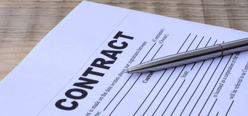 a sheet of paper with the word contract with a pen lies on a wooden table