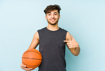 Young arabian man playing basket isolated person pointing by hand to a shirt copy space, proud and confident