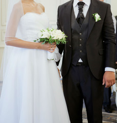 a young couple of European appearance, in classic wedding dresses, with a beautiful bouquet of snow-white flowers stand close to each other. Stability, simplicity, style, support, reliability