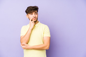 Young arabian man isolated on a purple background looking sideways with doubtful and skeptical expression.