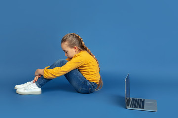 Portrait of sad little girl sitting isolated on blue studio background. How it feels to be autist....