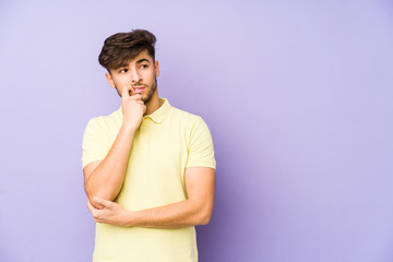 Young arabian man isolated on a purple background relaxed thinking about something looking at a copy space.