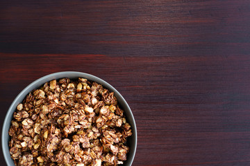 Homemade cocoa granola with crunchy peanuts and maple syrup in grey ceramic bowl. Morning light, red wooden table, high resolution