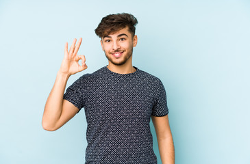 Young arabian man isolated on a blue background cheerful and confident showing ok gesture.