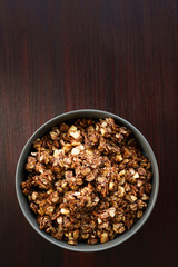 Homemade cocoa granola with crunchy peanuts and maple syrup in grey ceramic bowl. Morning light, red wooden table, high resolution