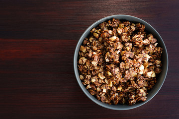 Homemade cocoa granola with crunchy peanuts and maple syrup in grey ceramic bowl. Morning light,...