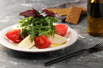 Salad of juicy, red, large tomatoes and buffalo mozzarella, with arugula and seasoned with olive oil.Decorated with basil.