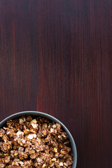 Homemade cocoa granola with crunchy peanuts and maple syrup in grey ceramic bowl. Morning light, red wooden table, high resolution