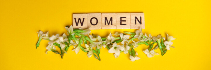 Top view word women spelled in wooden blocks on yellow background with flowers beneath them. Love,...