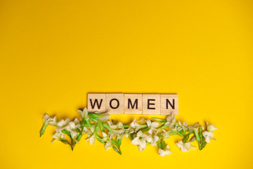 Top view word women spelled in wooden blocks on yellow background with flowers beneath them. Love,...