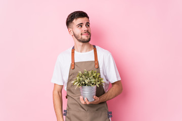 Young caucasian gardener man holding a plant isolated dreaming of achieving goals and purposes