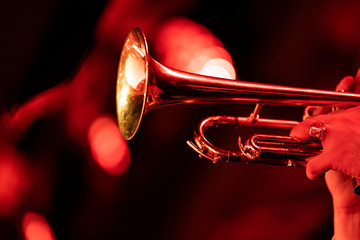 A trumpet player playing the trumpet in a big band concert on stage with red stage lights with bokeh in the background - obrazy, fototapety, plakaty