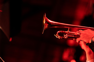 A trumpet player playing the trumpet in a big band concert on stage with red stage lights