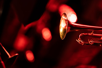A trumpet player playing the trumpet in a big band concert on stage with red stage lights with...