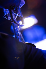 A trumpet section member of a big band resting before playing on stage with blue lights and a bright music stand light in front of him