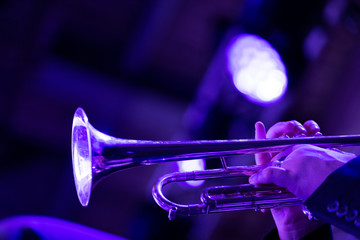 A big band member of the trumpet section is playing a solo during a performance on stage in purple lights