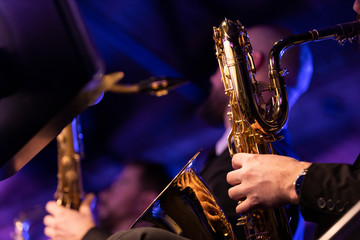 A baritone saxophone player playing their horn during a jazz concert in a venue with blue and...