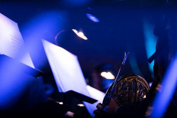 A French horn player holding their instrument during rests of a pops concert with blue streaks of...