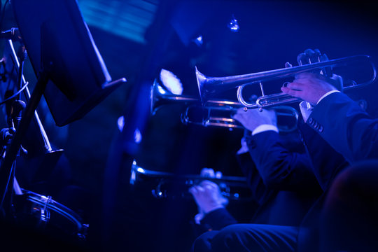 Members of a trumpet section of a big band playing a live show of jazz music on stage in blue stage lights