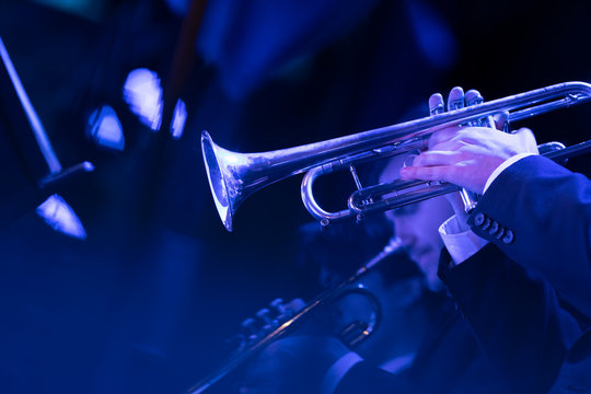 Members of a trumpet section of a big band playing a live show of jazz music on stage in blue stage lights