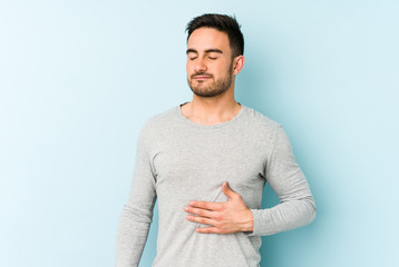 Young caucasian man isolated on blue background touches tummy, smiles gently, eating and...