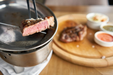 The waiter is holding a plate Grilled striploin steak with Pickled cabbage and two sauces. The strip steak, also called a New York strip. Serving on a wooden Board. Barbecue restaurant menu.