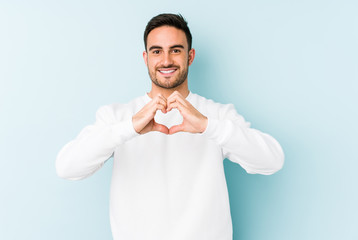 Young caucasian man isolated on blue background smiling and showing a heart shape with hands.