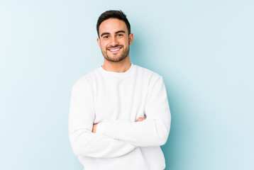 Young caucasian man isolated on blue background who feels confident, crossing arms with...