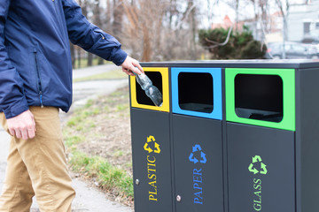 Hand of man throwing plactic bottle into trash bin for plastic waste. Modern colorful refuse bins...