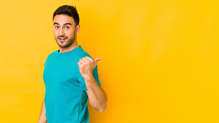 Young caucasian man isolated on yellow bakground points with thumb finger away, laughing and carefree.