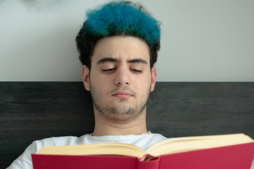 Close-up of a teenager reading, intrigued, a red book in his bed