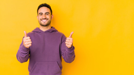 Young caucasian man isolated on yellow bakground smiling and raising thumb up