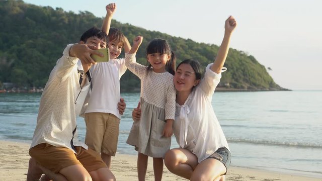 Happy asian family taking a picture with phone on the beach in vacation together, parents and children go to travel taking a photo for leisure and activity in summer, lifestyle concept.