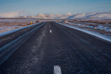 Straight winter road in Iceland with snow covered mountains 