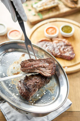 The waiter is butchering griled meat with a knife. Grilled fillet steaks with Pickled cabbage and two sauces.. Barbecue restaurant menu.