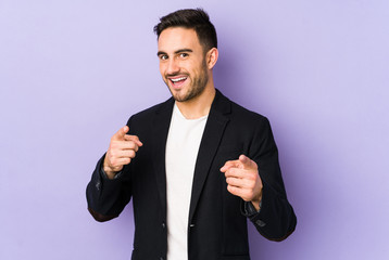 Young caucasian man isolated on purple background pointing to front with fingers.