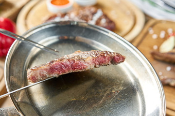 The waiter is holding a plate Grilled striploin steak with Pickled cabbage and two sauces. The strip steak, also called a New York strip. Serving on a wooden Board. Barbecue restaurant menu.