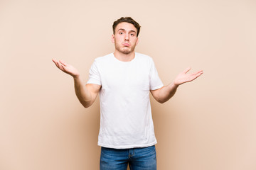 Young caucasian man posing isolated doubting and shrugging shoulders in questioning gesture.