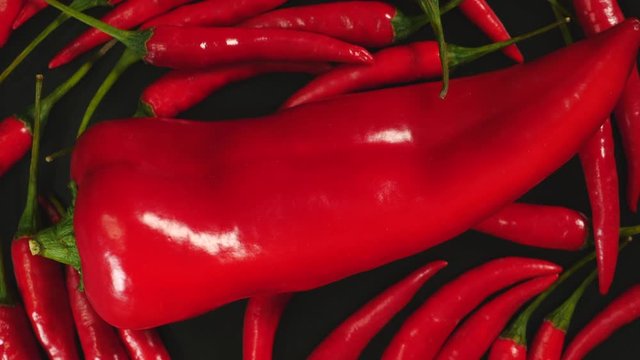 Top View Of Fresh Raw Red Chili Peppers And Ramiro Pepper Rotating On A Black Plate.