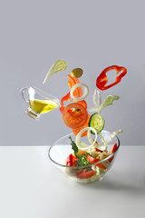 tomatoes, paprika, lettuce, cucumber slices, onions and other vegetables fall into a glass cup, olive oil, healthy eating concept